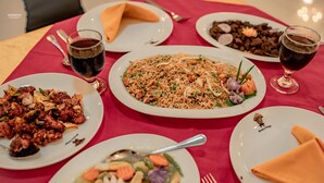 A table set with various dishes, including a large plate of rice, a salad, and a meat dish, along with two glasses of red wine. - G.M.T. Sorabora Village Hotel (Mahiyanganaya)
