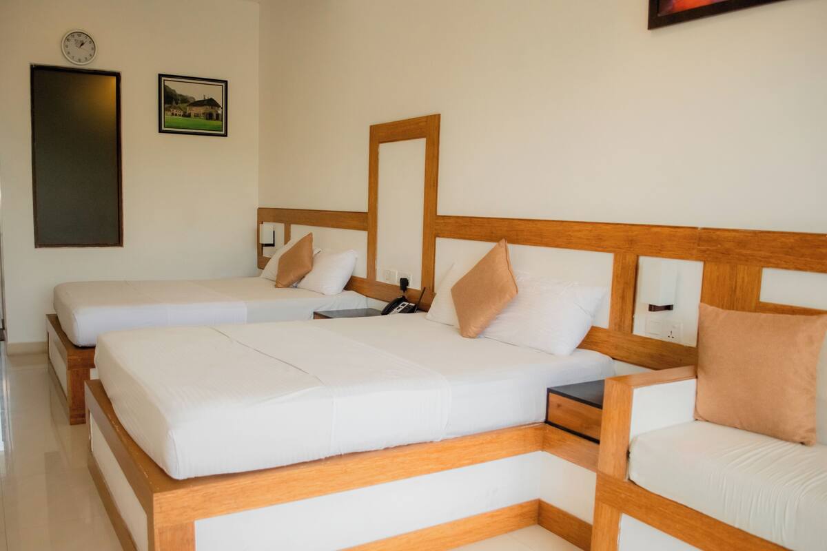 Ein Hotelzimmer mit zwei Einzelbetten, Holz-Kopfteilen, weißer Bettwäsche, einer Uhr und einem gerahmten Bild an der Wand.