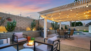 An outdoor patio area with a pergola, string lights, seating, and a fire feature. - Villa Solana: Heated Pool, Putting Green, Games (La Quinta)