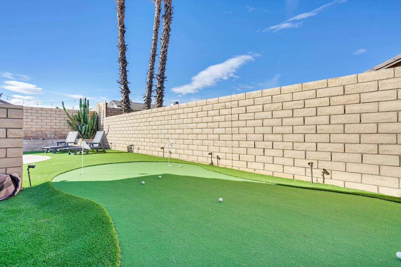 A miniature golf course with a brick wall, green artificial turf, and palm trees.