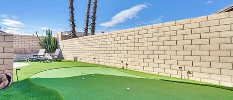 A miniature golf course with a brick wall, green artificial turf, and palm trees.