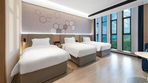 Une chambre d’hôtel moderne avec trois lits, une grande fenêtre offrant une belle vue et un mur orné de motifs hexagonaux.