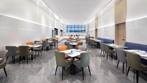 Un espace repas moderne, doté de tables et de chaises, d’une grande fenêtre et offrant une vue sur l’extérieur.