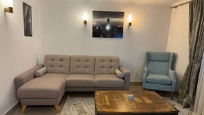 Un salon comprenant un canapé d’angle, un fauteuil bleu, une table basse et deux lampes fixées au mur.