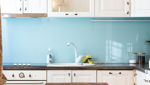Une cuisine de taille modeste, avec des meubles blancs, un pare-feu bleu, un évier blanc et une cuisinière.