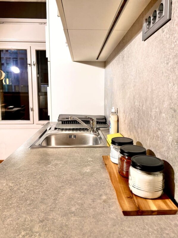 Una cocina con un lavamanos de acero inoxidable, una encimera de madera y frascos de especias.