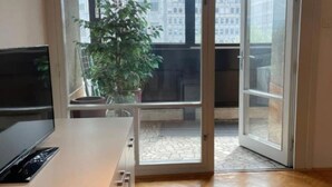 Ein Zimmer mit einer Schiebetür zum Balkon, einem Topfpflanzen und einem Flachbildfernseher auf einem weißen Schrank.