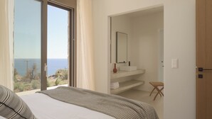 Ein Schlafzimmer mit großem Fenster, einem Bett, einem Nachttisch und Blick aufs Meer.