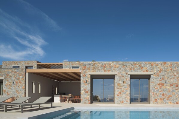 A modern building with a stone facade, a pool, and outdoor seating.
