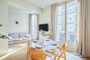 Un salon moderne comprenant un coin repas, de grandes fenêtres, un téléviseur à écran plat et une vue sur la ville.