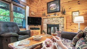 Un interior acogedor de cabaña con chimenea de piedra, sofás de cuero, un televisor y una mesa de centro de madera.