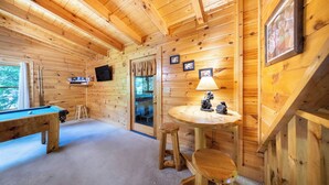 A wooden cabin interior with a pool table, a small round table with a lamp, and a television mounted on the wall. - Eagles Ridge Cabin · Hot Tub, Jacuzzi & Pool Table (Pigeon Forge)