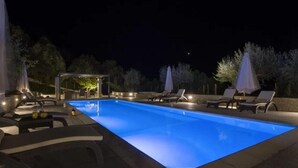 Une piscine entourée d’arbres, avec des chaises longues et des parasols, ainsi qu’un espace de repos abrité.