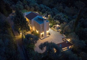 Una casa moderna con un patio de piedra, rodeada por un bosque denso.
