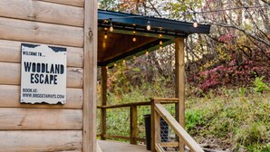 Una cabaña de madera con un cartel que dice "WELCOME TO WOODLAND ESCAPE" y un sitio web para reservas.