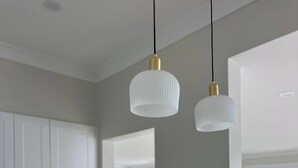 Una cocina moderna con armarios blancos, encimera blanca, grifo dorado y dos lámparas colgantes.