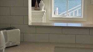 Una cocina con armarios blancos, un tostador y una ventana con vistas al océano.