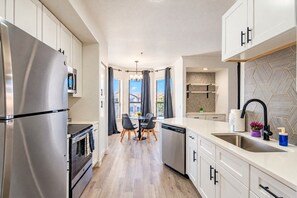 Une cuisine moderne équipée d’appareils électroménagers en acier inoxydable, un coin repas avec une table et des chaises, et une vue par la fenêtre.