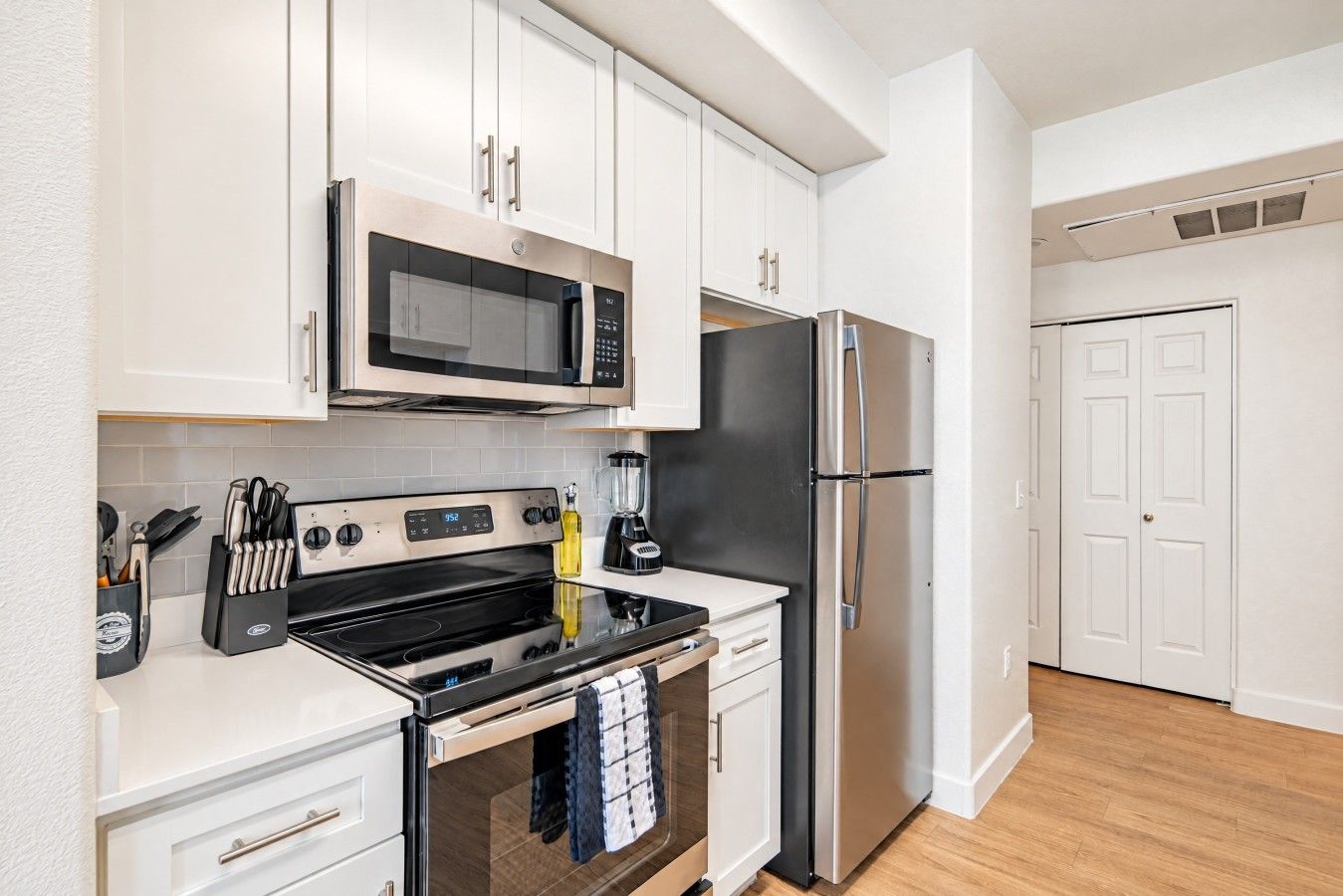A modern kitchen with stainless steel appliances, white cabinetry, and a black countertop.
