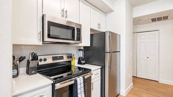 A modern kitchen with stainless steel appliances, white cabinetry, and a black countertop.