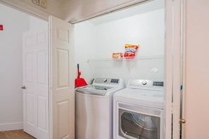 A laundry room with two front-loading washing machines and a dryer, a red mop, and laundry detergent on a shelf.