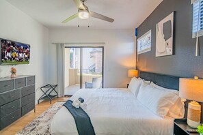 A hotel room with a bed, a TV, a desk, a chair, a window, and a ceiling fan.