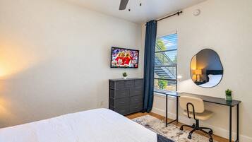 Un dormitorio con cama, escritorio, silla, cómoda, ventana con vistas y espejo.