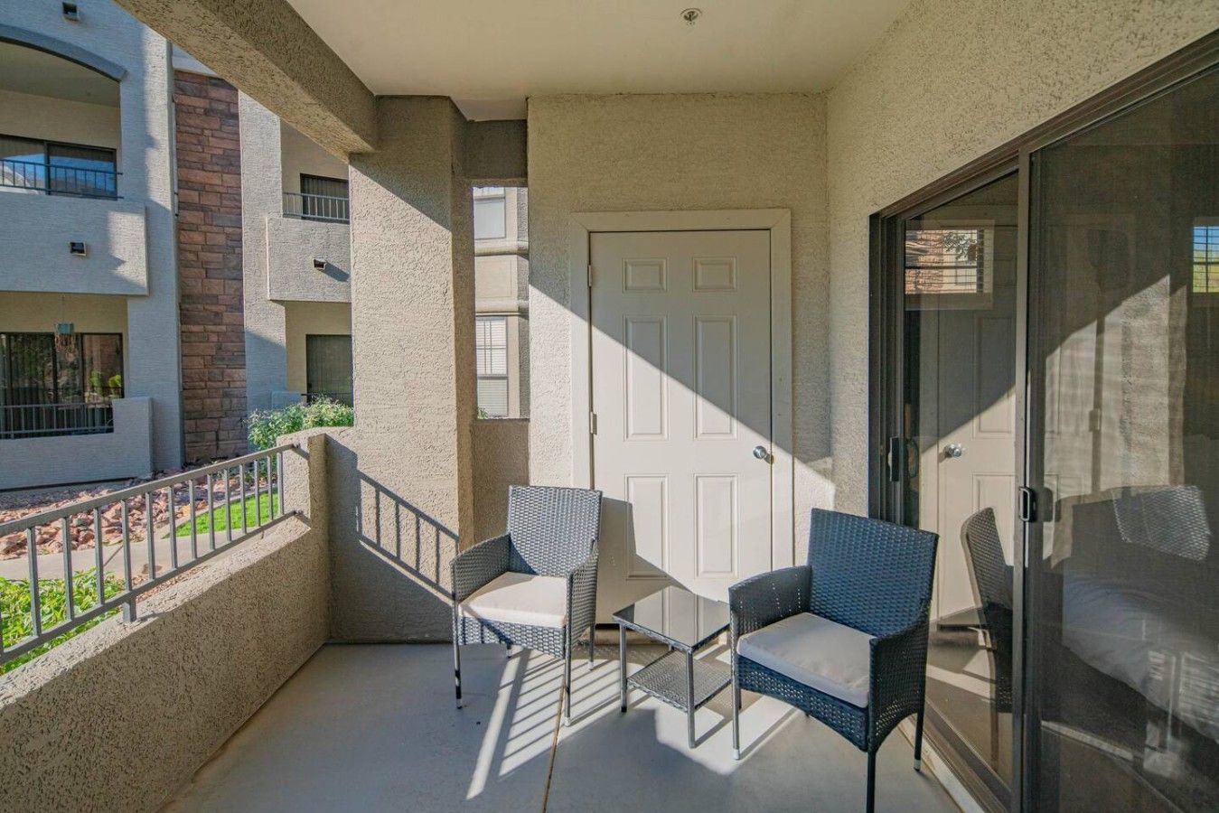 Un balcon avec deux fauteuils en osier, une porte blanche et une porte vitrée donnant sur le balcon.