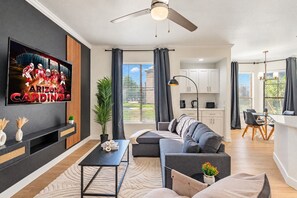 Una sala de estar moderna con una televisión de pantalla plana, un sofá, una mesa de centro y un comedor con una mesa y sillas.