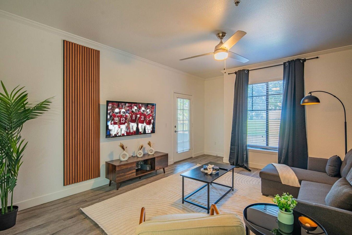 A modern living room with a flat-screen TV, a ceiling fan, a sofa, and a coffee table.