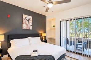 Habitación de hotel moderna con una cama grande, ventilador de techo, un cuadro en la pared y vistas al exterior a través de una puerta corrediza.