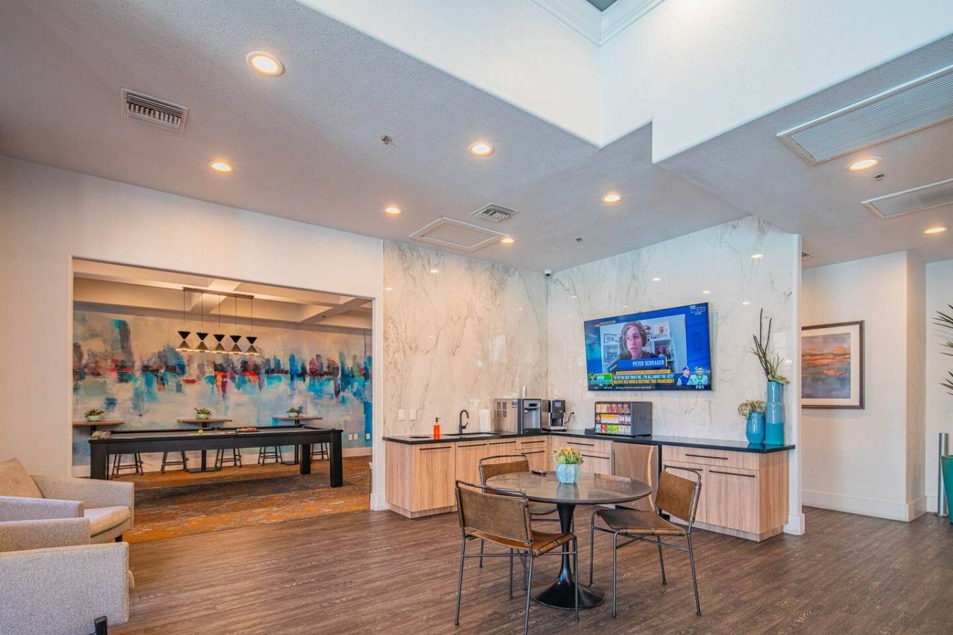 A modern kitchen with a marble countertop, a television mounted above the island, and a dining area with a round table and chairs.