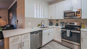 A modern kitchen with white cabinets, stainless steel appliances, a dishwasher, and a window with patterned glass. - Near the Stadium with  Pool Gym Parking HotTub WD (Glendale)