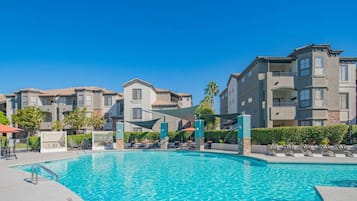 A swimming pool with lounge chairs and a covered area, surrounded by multi-story residential buildings.