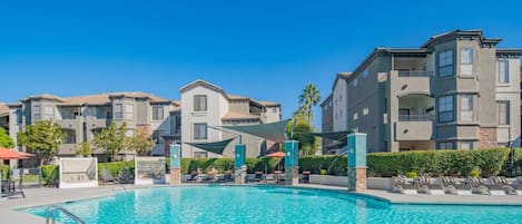A swimming pool with lounge chairs and a covered area, surrounded by multi-story residential buildings.