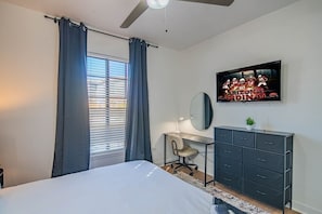 Quarto com cama, escrivaninha, cômoda, ventilador de teto e TV exibindo o Arizona Cardinals.