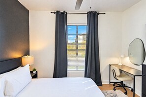 Una camera da letto con un letto, una scrivania con una sedia, uno specchio e una finestra con tende.