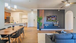A modern apartment with a dining area, kitchen, living room, and a large TV mounted on the wall.