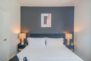 Ett hotellrum med en säng, två sängbord med lampor, en dörr och ett konstverk som hänger på väggen.