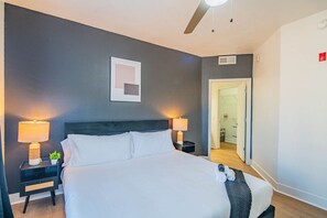 A hotel room with a bed, two bedside tables with lamps, a ceiling fan, a framed picture on the wall, and a door leading to a bathroom. - Near State Farm Stadium with Pool, Gym, Balcony, W (Glendale)