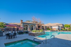 A pool area with lounge chairs and umbrellas, a barbecue grill, and a building with a stone facade. - Near State Farm Stadium with Pool, Gym, Balcony, W (Glendale)