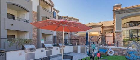 An outdoor patio with a grill, seating area, and a swing chair.