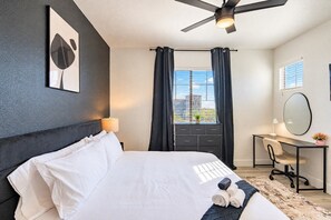 Habitació d'hotel moderna amb un llit, escriptori, cadira, ventilador de sostre, finestra amb cortines i un mirall fixat a la paret.