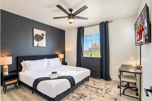 A modern hotel room with a large bed, a desk, a chair, a ceiling fan, a TV, and a window with curtains. - Near Attractions |Balcony, Pool, Gym, Parking, W/D (Glendale)