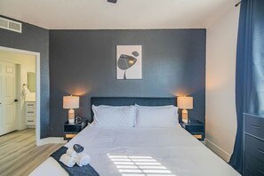 A hotel room with a large bed, two bedside lamps, a wall-mounted artwork, and a view of the hallway. - Near Attractions |Balcony, Pool, Gym, Parking, W/D (Glendale)