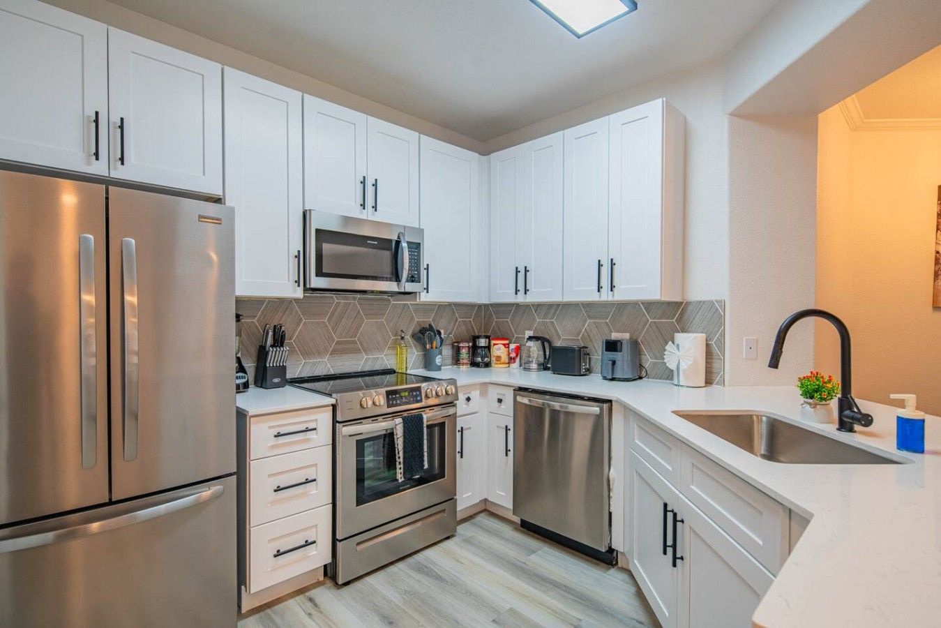 A modern kitchen with stainless steel appliances, white cabinetry, and a herringbone tile backsplash.