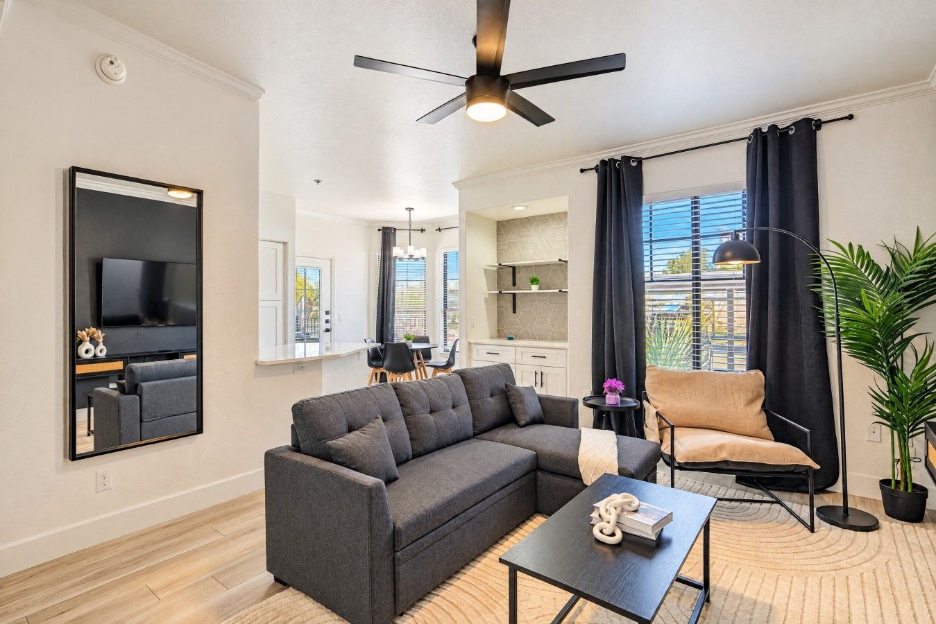 Un salon moderne avec un canapé d’angle, un téléviseur à écran plat, un ventilateur de plafond et un coin repas à l’arrière-plan.