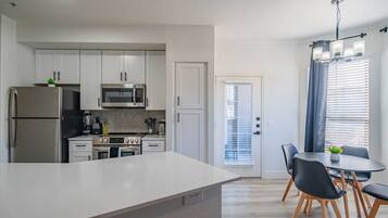 Une cuisine moderne avec des meubles blancs, des appareils en acier inoxydable et un coin repas comprenant une table et des chaises.