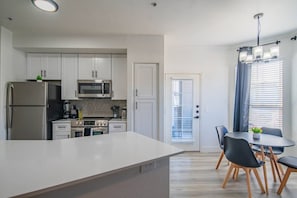 A modern kitchen with white cabinetry, stainless steel appliances, and a dining area with a table and chairs.