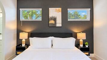 A bedroom with a large bed, two bedside tables with lamps, and three framed pictures on the wall.